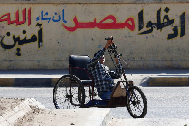 Homem com decifiência dirige uma motocicleta em frente a um muro com os dizeres "Entre, o Egito é seguro", próximo ao local de uma explosão em Cairo, Egiro - 09/12/2016