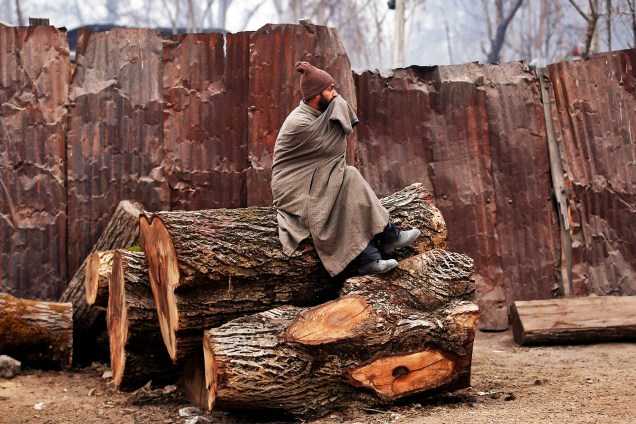 Homem se senta em tronco de árvore, em uma manhã de inverno na região de Srinagar, na Índia - 15/12/2016