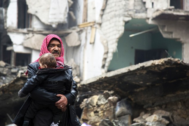 Homem sírio carrega criança próximo a prédios destruídos, durante operação militar em Alepo - 13/12/2016