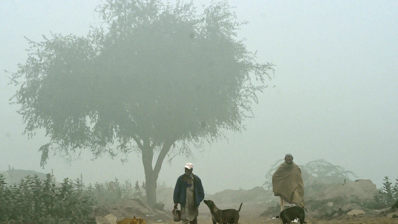 Homens caminham em um campo enevoado em Lahore, no Paquistão