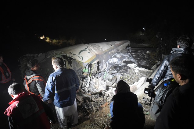 Oficiais da companhia Pakistan International Airlines observam destroços do avião no local do acidente, no Paquistão