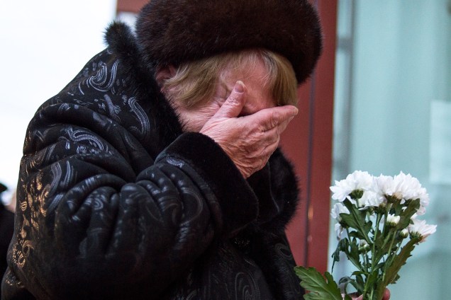 Mulher deposita flores no edifício do conjunto de Alexandrov (Coro do Exército Vermelho), em homenagem às vítimas do coral que estavam no avião militar russo que caiu neste domingo (25)