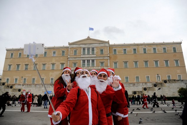 Pessoas vestidas de papai noel tiram uma selfie na frente do edifício do parlamento em Atenas, na Grécia