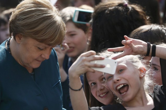 Crianças fazem selfies enquanto a chanceler alemã, Angela Merkel assina autógrafos durante visita a uma escola secundária francesa em Berlim