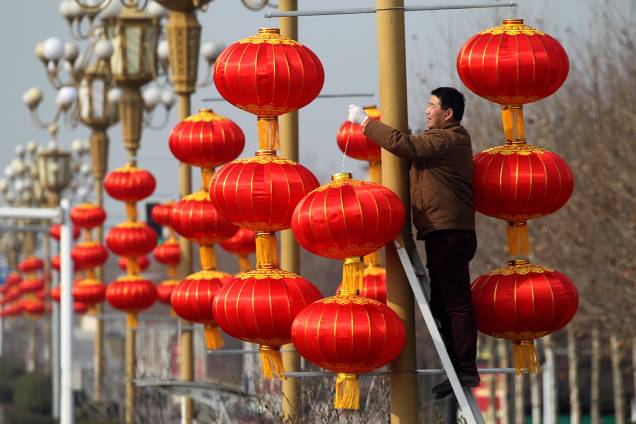 Homem pendura lanternas em postes para comemorar o ano novo chinês no calendário lunar, na China Homem pendura lanternas em postes para comemorar o ano novo chinês no calendário lunar, na China