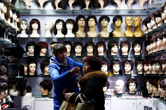 Vendedora coloca peruca em cliente, em uma loja próxima da estação ferroviária de Xangai, na China - 18/01/2017
