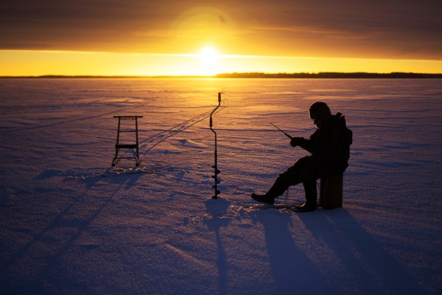 Homem pesca em lago congelado de Vaasa, na Finlândia, durante pôr do sol - 17/01/2017