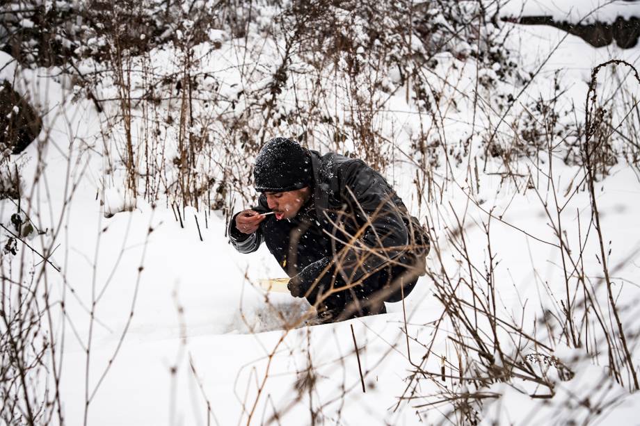 Migrante se alimenta sentado na neve em Belgrado, na Sérvia - 11/01/2017