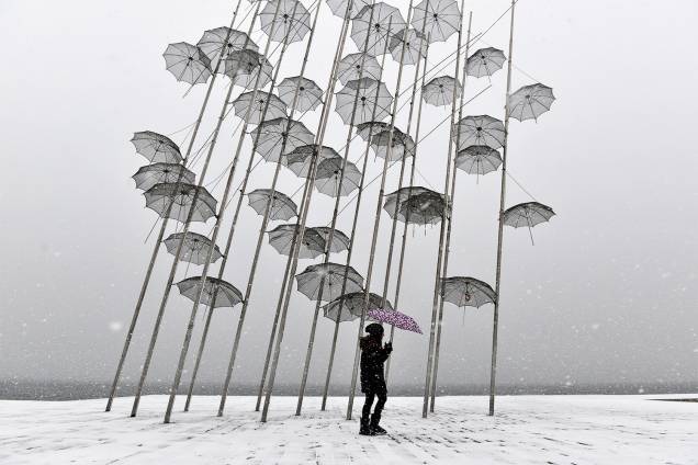 Homem carrega guarda-chuva enquanto caminha próximo da escultura do artista grego George Zongolopoulos, durante forte nevasca na cidade de Salonica - 10/01/2017