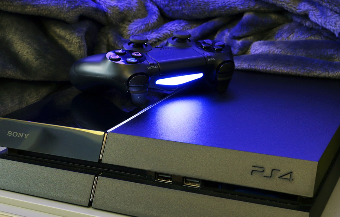 Ancona, Italy - February 18, 2015: Sony Playstation 4 and black wireless DualShock 4 controller on a desk. The PlayStation 4, registered trademark PLAYSTATION 4 is a video game console produced by Sony Computer Entertainment and is part of the eighth generation of consoles.