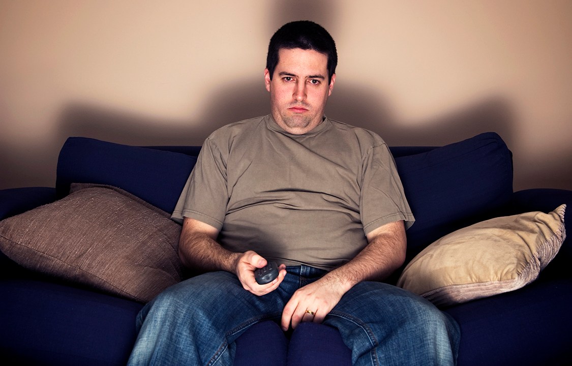 Bored, lazy, overweight man sits on the sofa