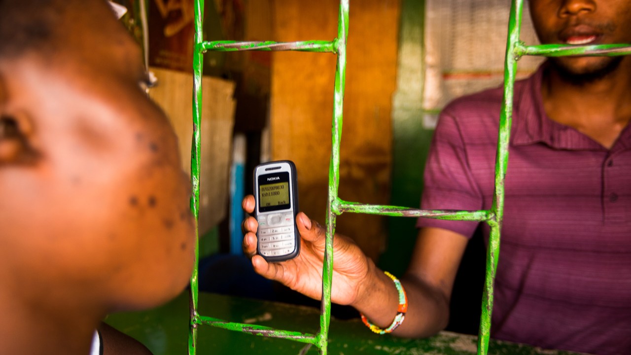 Agente credenciado do serviço M-Pesa, da Safaricomm, mostra a tela do celular para um cliente de Nairóbi, no Quênia, para comprovar que a transferência de dinheiro foi realizada, em abril de 2013