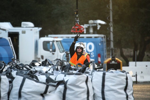 Trabalhador pendura sacos com pedra em helicóptero para <span>reparar o solo próximo ao escoadouro de emergência da barragem de Oroville, Califórnia, na tentativa de evitar o rompimento do sistema de contenção da represa</span> - 13/02/2017