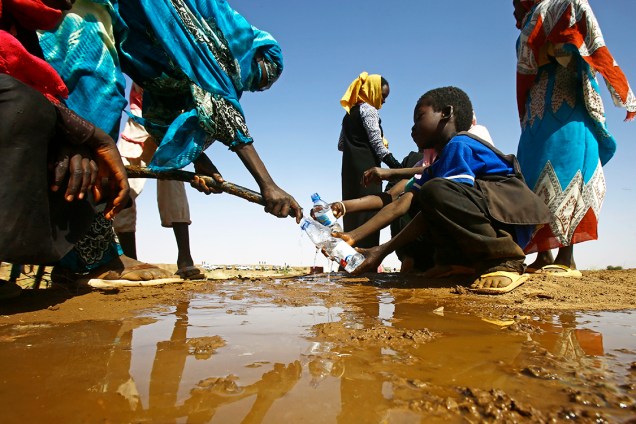 Mulher enche uma garrafa com água, no Sudão