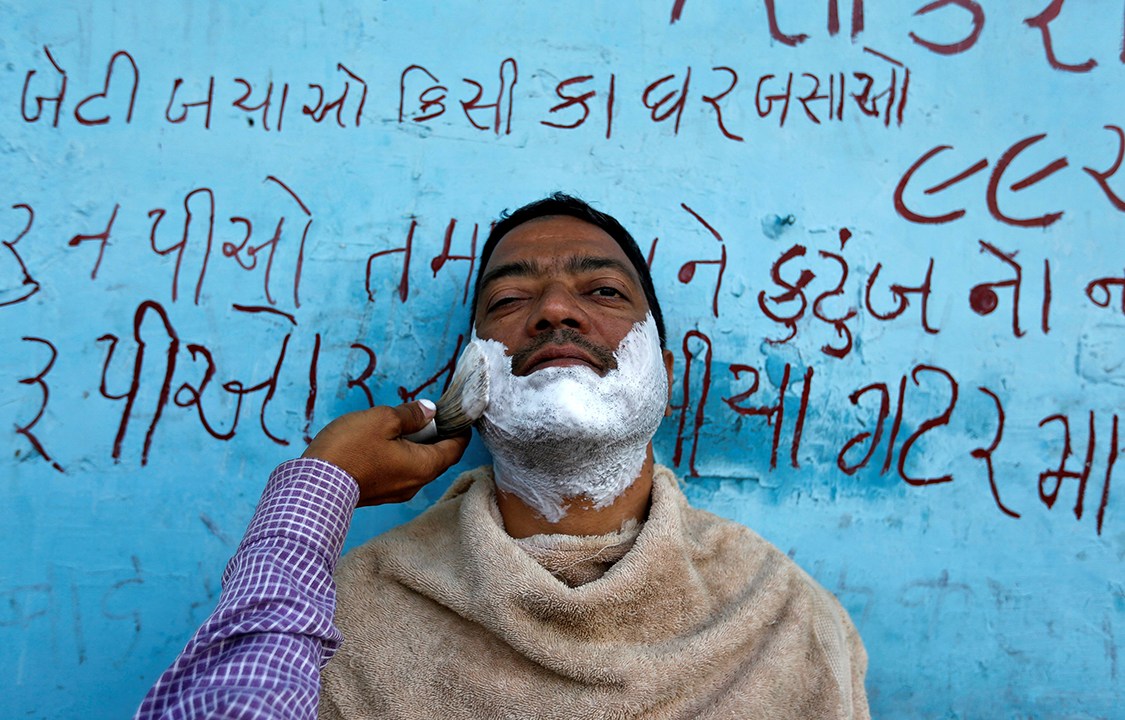 Homem faz a barba em uma estrada na cidade de Ahmedabad, na Índia