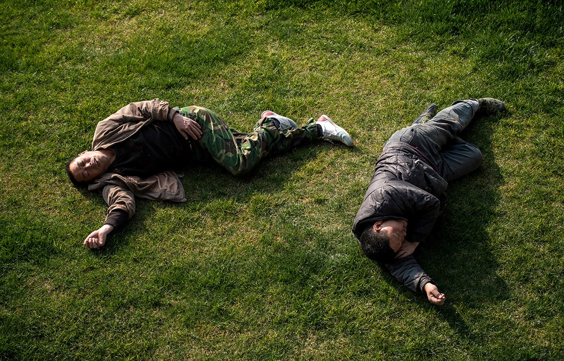 Dois trabalhadores cochilam em um campo aberto em frente à estação de trem de Shanghai, na China