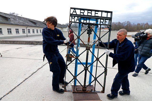Homens carregam portão de ferro original de um campo de concentração com o famoso slogan nazista "O trabalho liberta" em Dachau, Alemanha- 22/02/2017