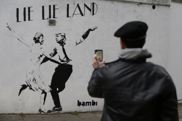 Homem tira uma foto de um mural do artista britânico Bambi satirizando a primeira-ministra britânica Theresa May e o presidente dos Estados Unidos, Donald Trump, em Londres - 23/02/2017