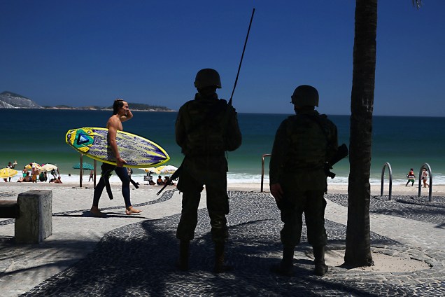 Surfista passa por soldados do exército que fazem a segurança na praia do Arpoador, RJ - 15/02/2017