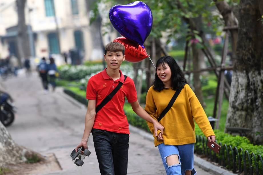 Casal caminha carregando balões em formato de coração durante comemorações do dia de São Valentim, o "Valentine's Day"