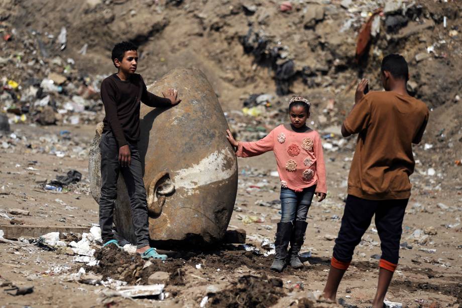 Crianças fazem fotos próximas a cabeça de uma estátua do faraó Ramsés II encontrada por trabalhadores em uma favela no Cairo - 09/03/2017