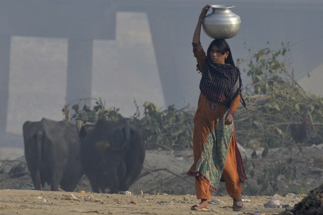 Mulher carrega um recipiente com água sobre cabeça nos subúrbios de Lahore, no Paquistão - 21/03/2017