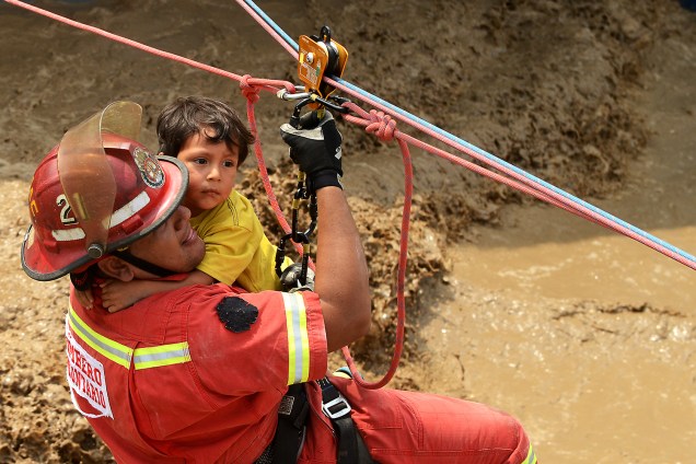 Menino é ajudado por um bombeiro após enchentes e deslizamentos na cidade de Huachipa. Os incidentes provocados pelo fenômeno climático<span>"el niño costero"</span> já mataram dezenas de pessoas no Peru - 17/03/2017