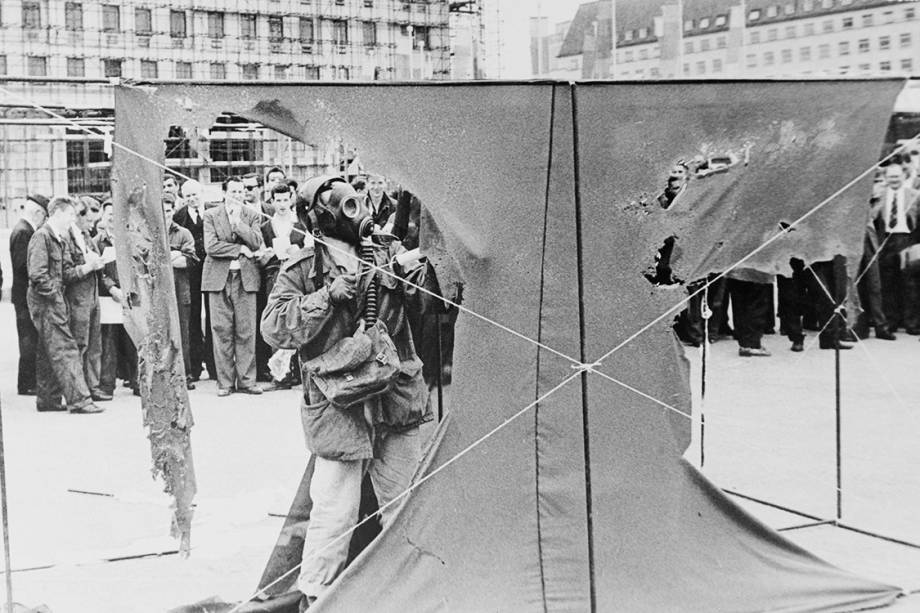 O artista alemão Gustav Metzger veste uma máscara de gás enquanto pinta cortinas de nylon com ácido clorídrico, fazendo com que se desintegram, em 1961