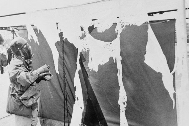 O artista alemão Gustav Metzger veste uma máscara de gás enquanto pinta cortinas de nylon com ácido clorídrico, fazendo com que se desintegram, em 1961