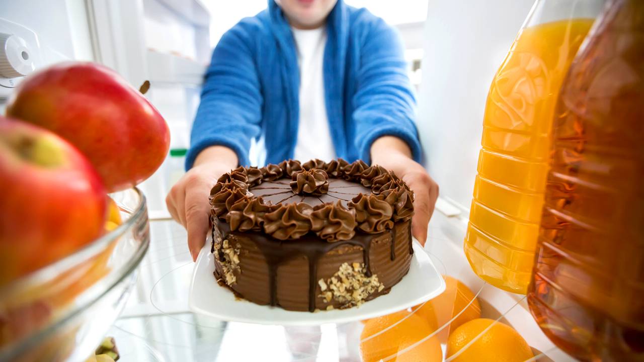 Homem pega bolo de chocolate na geladeira