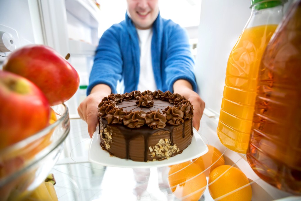 Homem pega bolo de chocolate na geladeira