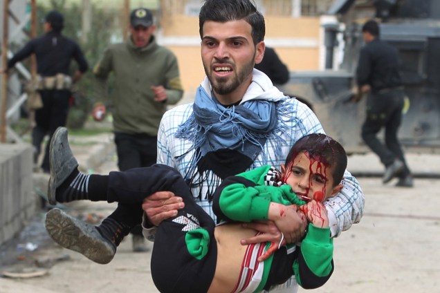 Homem carrega um menino ferido após ataque atribuído a jihadistas do Estado Islâmico sobre civis no bairro de Al-Risala, em Mosul, no Iraque