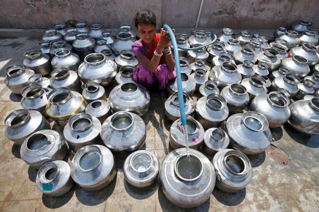 Menina enche os jarros de metal com água do lado de fora de um templo em Ahmedabad, na India - 30/03/2017