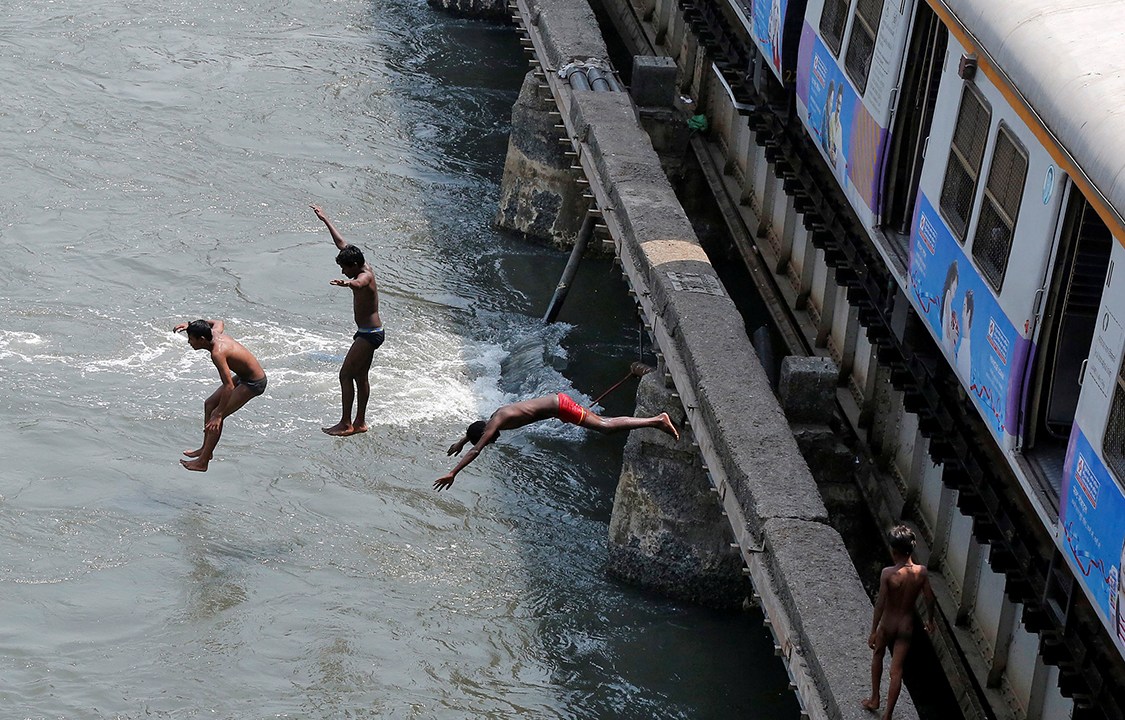 Garotos pulam de uma plataforma de trem para um rio, em um dia quente de verão na cidade de Mumbai, Índia