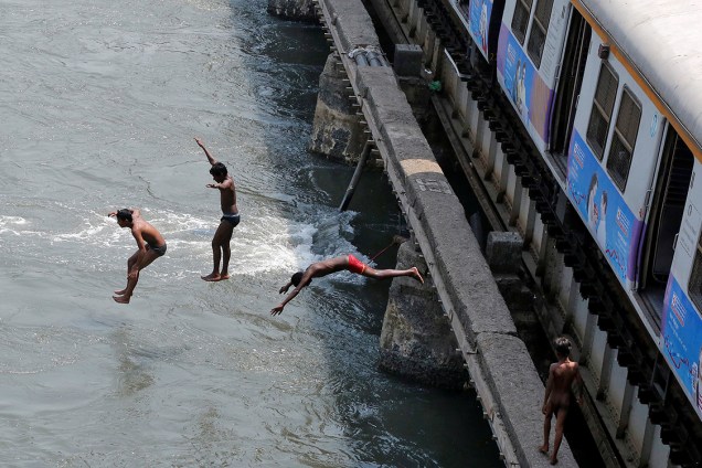 Garotos pulam de uma plataforma de trem para um rio, em um dia quente de verão na cidade de Mumbai, Índia - 31/03/2017