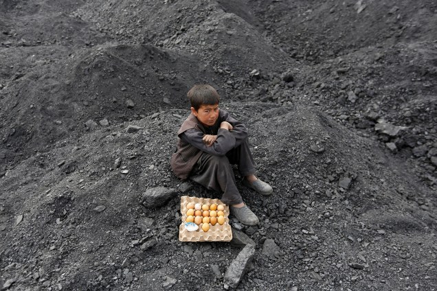 Menino vendedor de ovos cozidos espera por clientes em um local de despejo de carvão nos arredores de Cabul, no Afeganistão - 07/03/2017