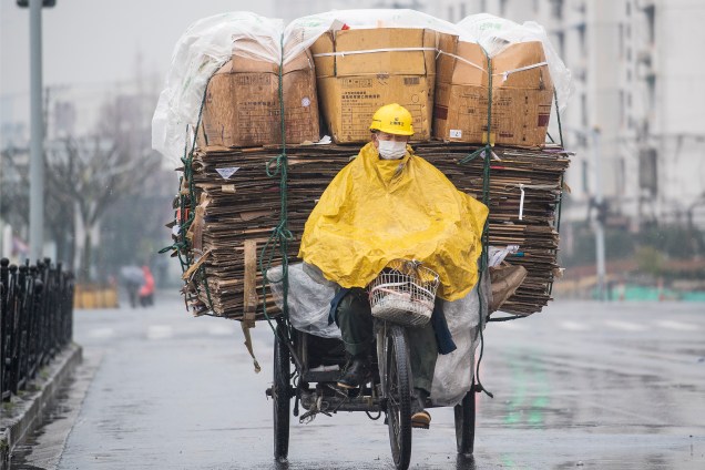 Trabalhador se protege com uma capa de chuva enquanto pedala em seu triciclo carregado de papéis para reciclagem em Xangai, na China - 13/03/2017