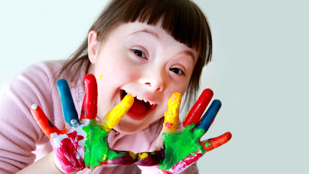 Menina com Síndrome de Down com tinta colorida nas mãos