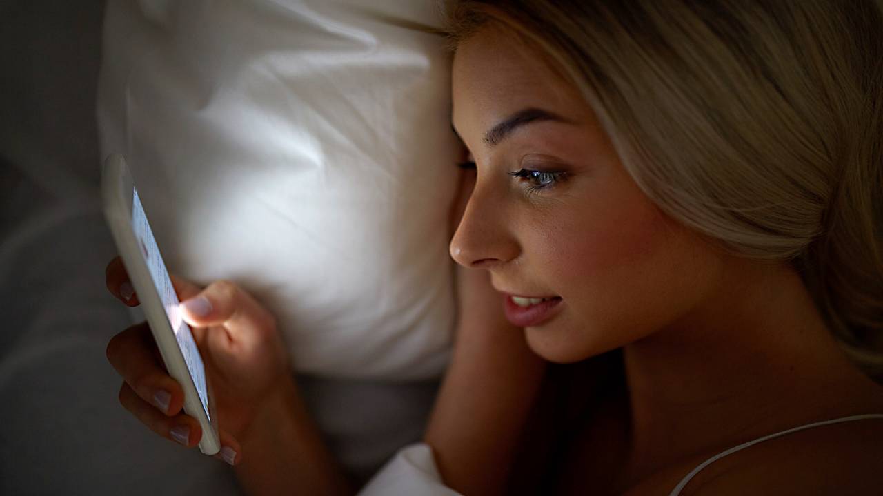Mulher deitada na cama mexendo no celular