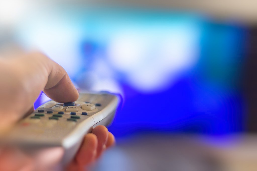 Close up of remote in hand with shallow depth of field during television watching