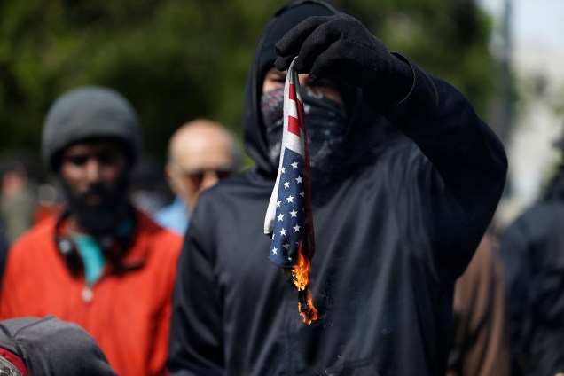 Manifestante queima bandeira dos Estados Unidos em protesto contra decisões fiscais de Donald Trump, em Berkeley, Califórnia