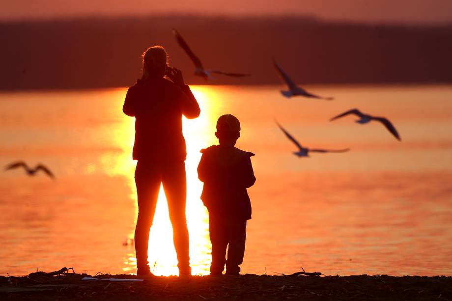 Mãe e filho fotografam pôr-do-sol em um lago na cidade de Minsk, Belarus