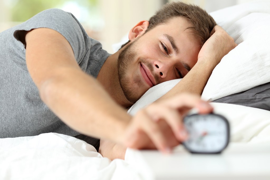 Homem acordando feliz e desligando o despertador