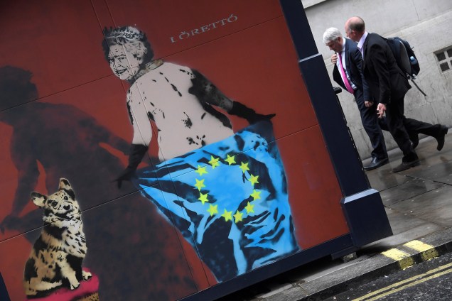 Pedestres caminham perto de um grafite com a imagem da rainha Elizabeth II com um cão estimação, segurando uma bandeira da União Europeia em Londres - 24/04/2017