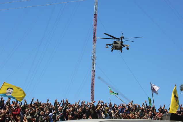 Curdos acenam bandeiras enquanto um helicóptero médico, da coalizão liderada pelos Estados Unidos, sobrevoa o local de ataques aéreos turcos perto da cidade curda de Derik, no nordeste da Síria - 25/04/2017