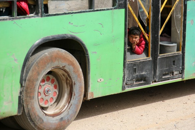 Menino é fotografado em um ônibus com civis das cidades de Fuaa e Kafraya, que está sob um cerco há mais de dois anos, enquanto esperam no ponto de trânsito de Rashidin, mantido pelos rebeldes nos arredores de Aleppo, na Síria - 21/04/2017