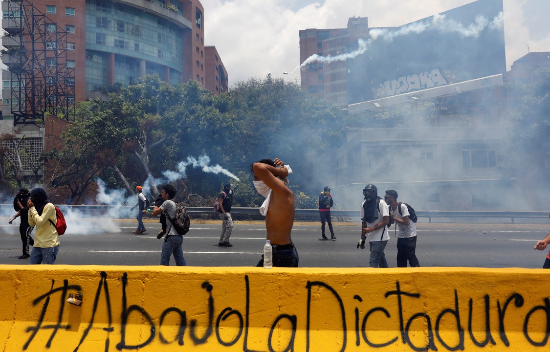 Manifestantes se protegem das bombas de gás lacrimgêneo lançadas pela polícia durante protesto contra o presidente Nicolás Madura, em Caracas, na Venezuela