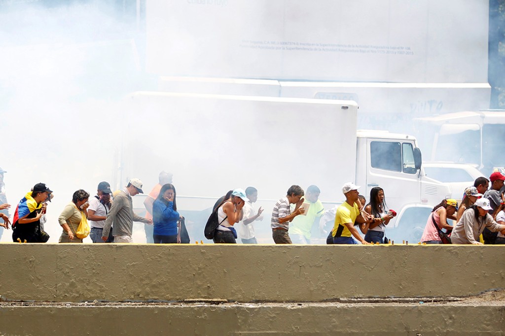 Manifestantes se protegem das bombas de gás lacrimgêneo lançadas pela polícia durante protesto contra o presidente Nicolás Madura, em Caracas, na Venezuela