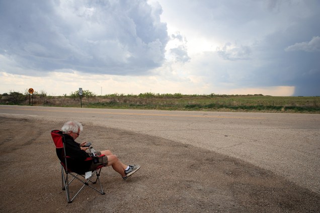 O meteorologista Josh Wurman, presidente de fundados do Centro de Pesquisas de Climas Severos, senta à beira da estrada enquanto acompanha pelo seu celular a formação de uma tempestade em Portales, Novo México