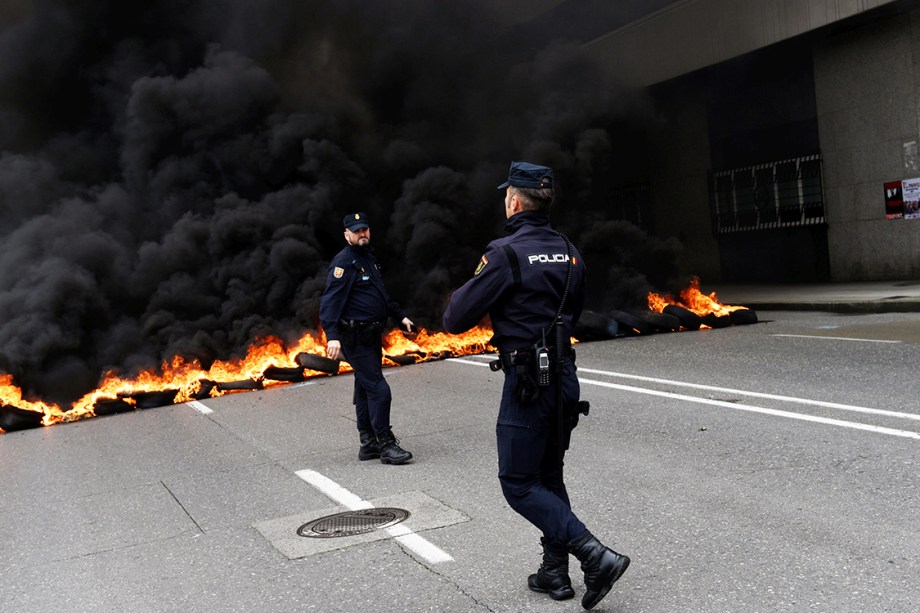 Policiais caminham em frente a uma barricada feita por manifestantes durante protestos do Dia do Trabalho em Gijón, Espanha